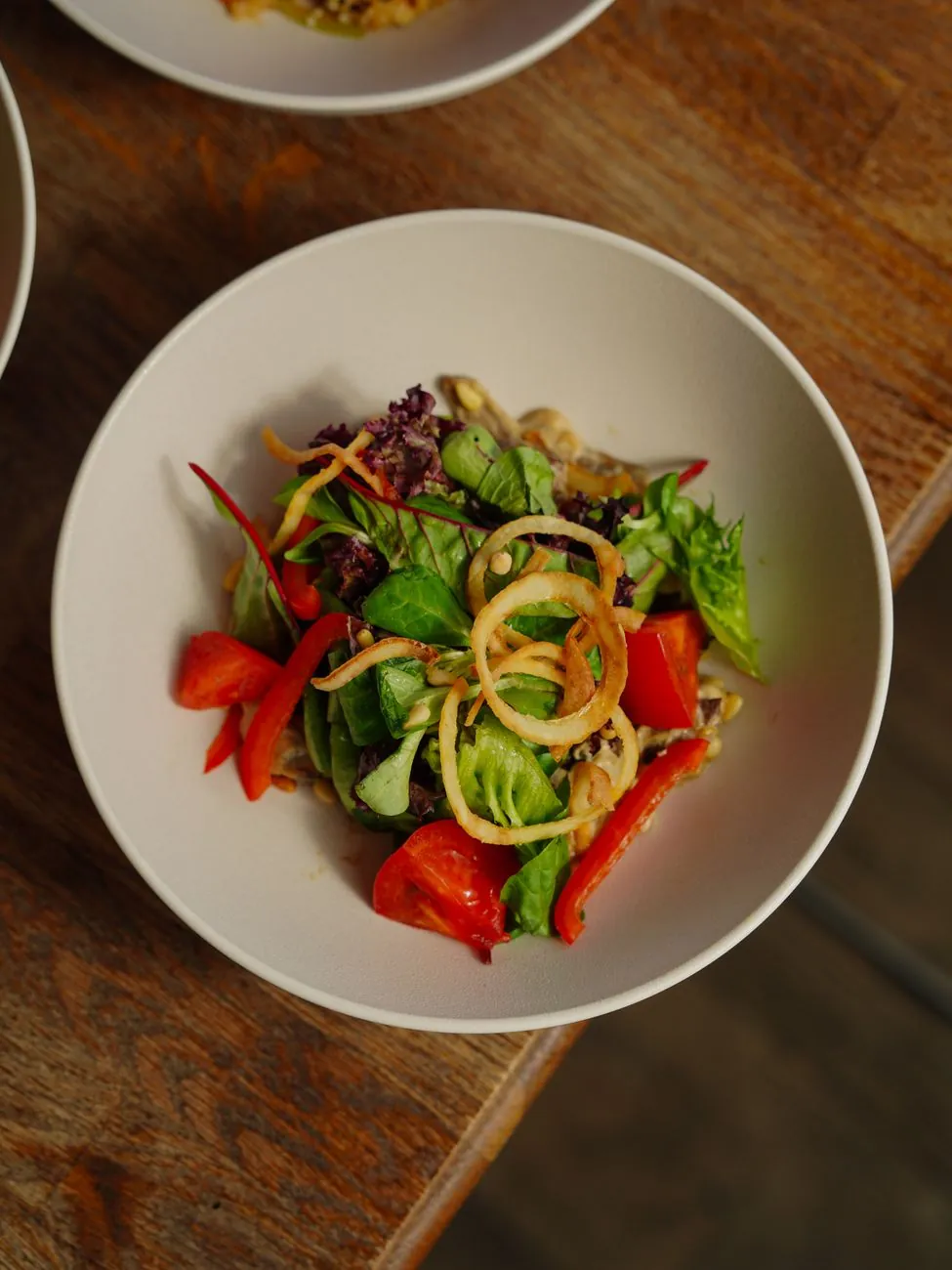 Bát salad rau xanh với cà chua và ớt chuông nhìn từ trên xuống trên bàn gỗ